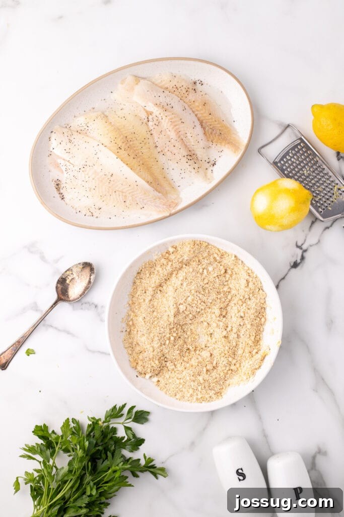 Raw flounder fillets seasoned with black pepper next to a bowl of breadcrumb and parmesan mixture with parsley and lemons, ready for coating.