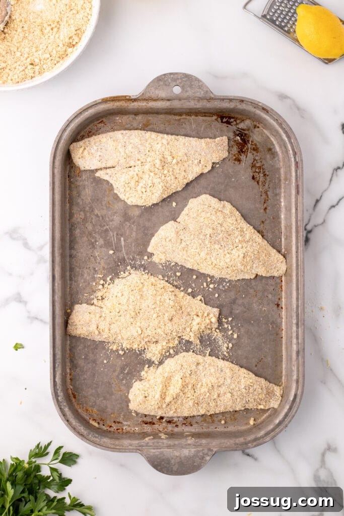 Breaded flounder fillets arranged neatly on a baking sheet before baking, showing preparation for the oven.