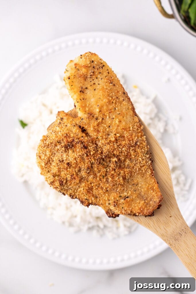 Cooked breaded flounder fillet on a wooden spatula over a plate of white rice, showing the serving suggestion.