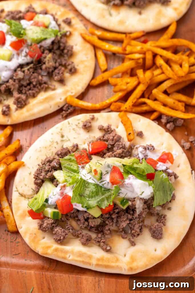 Hafta İçi Akşamlarına Özel Kolay Yunan Kıymalı Pide 2 Close view of pita bread topped with savory ground beef, a generous dollop of creamy yogurt sauce, fresh cucumber, ripe tomato, and crisp lettuce, ready to be enjoyed.