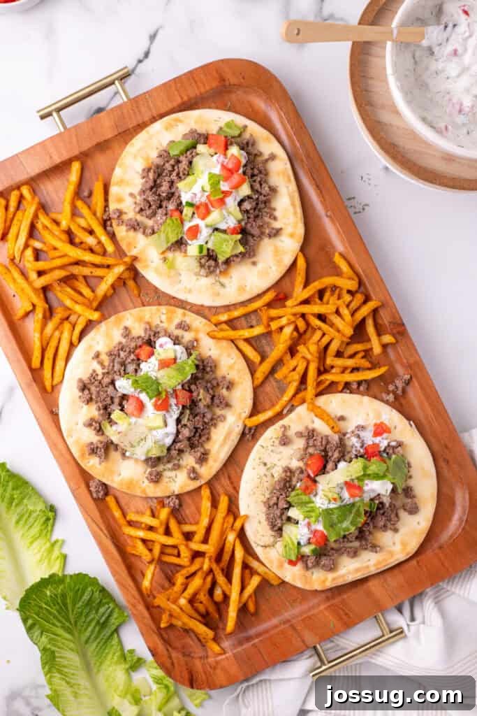 Hafta İçi Akşamlarına Özel Kolay Yunan Kıymalı Pide 15 Another close-up shot of a Greek Ground Beef Pita, featuring the rich beef, creamy sauce, and colorful vegetables, presented on a wooden tray.