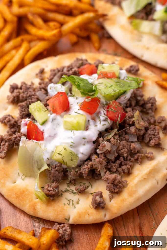 Hafta İçi Akşamlarına Özel Kolay Yunan Kıymalı Pide 17 A final close-up of a mouthwatering Greek Ground Beef Pita, generously topped with creamy yogurt sauce, fresh cucumber, ripe tomato, and crisp lettuce, served with a side of golden fries.