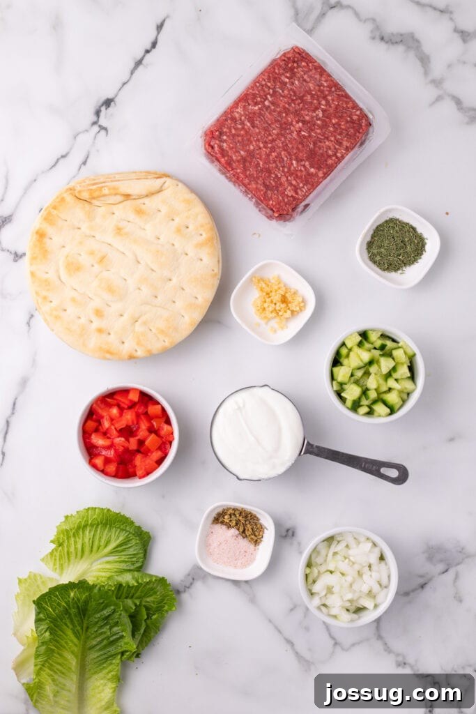 Hafta İçi Akşamlarına Özel Kolay Yunan Kıymalı Pide 3 An array of fresh ingredients for Greek Ground Beef Pitas displayed on a marble surface: fluffy pita bread, raw lean ground beef, finely chopped tomatoes, crisp cucumber, pungent onion, aromatic garlic, creamy Greek yogurt, fresh lettuce, and a sprinkle of dried herbs.