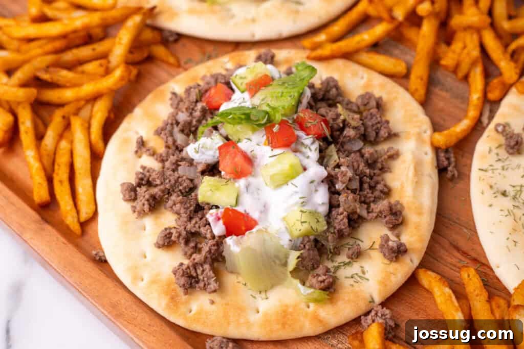 Hafta İçi Akşamlarına Özel Kolay Yunan Kıymalı Pide 4 A close-up view of a perfectly crafted Greek Ground Beef Pita, showcasing the seasoned meat, creamy yogurt sauce, fresh cucumber, ripe tomato, and crisp lettuce, elegantly arranged on a rustic wooden tray.