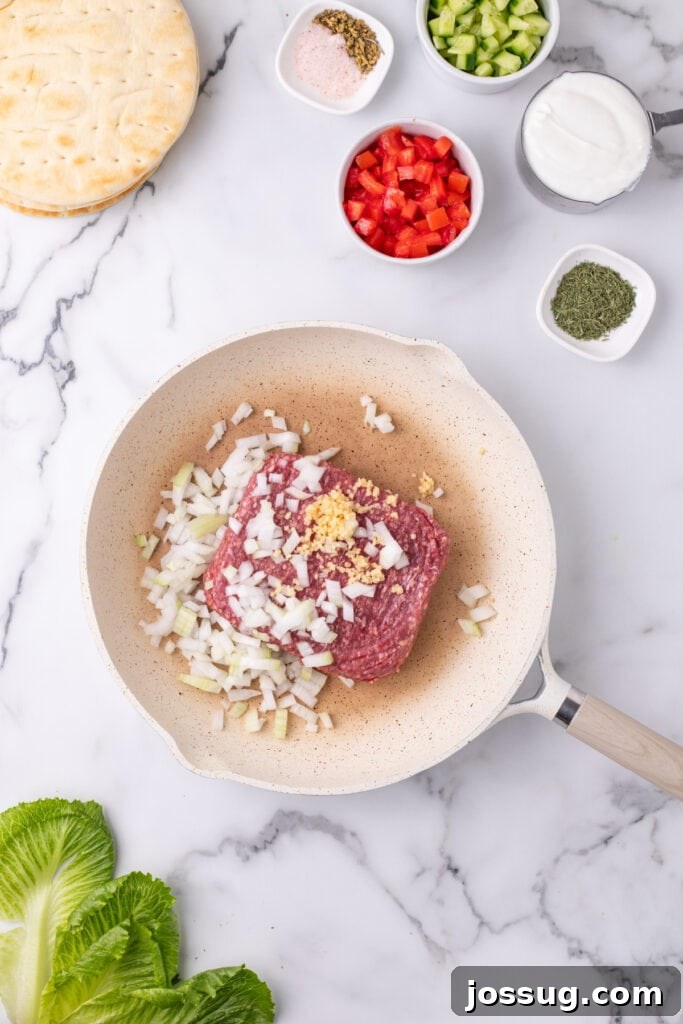 Hafta İçi Akşamlarına Özel Kolay Yunan Kıymalı Pide 5 Raw ground beef cooking in a skillet with chopped onion and minced garlic on a marble surface, beginning to brown.