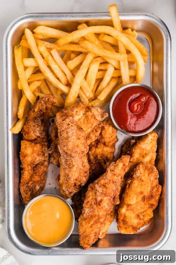 Effortless Crispy Chicken Strips for Busy Families 2 Crispy golden fried chicken strips served with a generous portion of fries and a dollop of vibrant red ketchup in a rustic metal tray, ready for a comforting and satisfying meal.