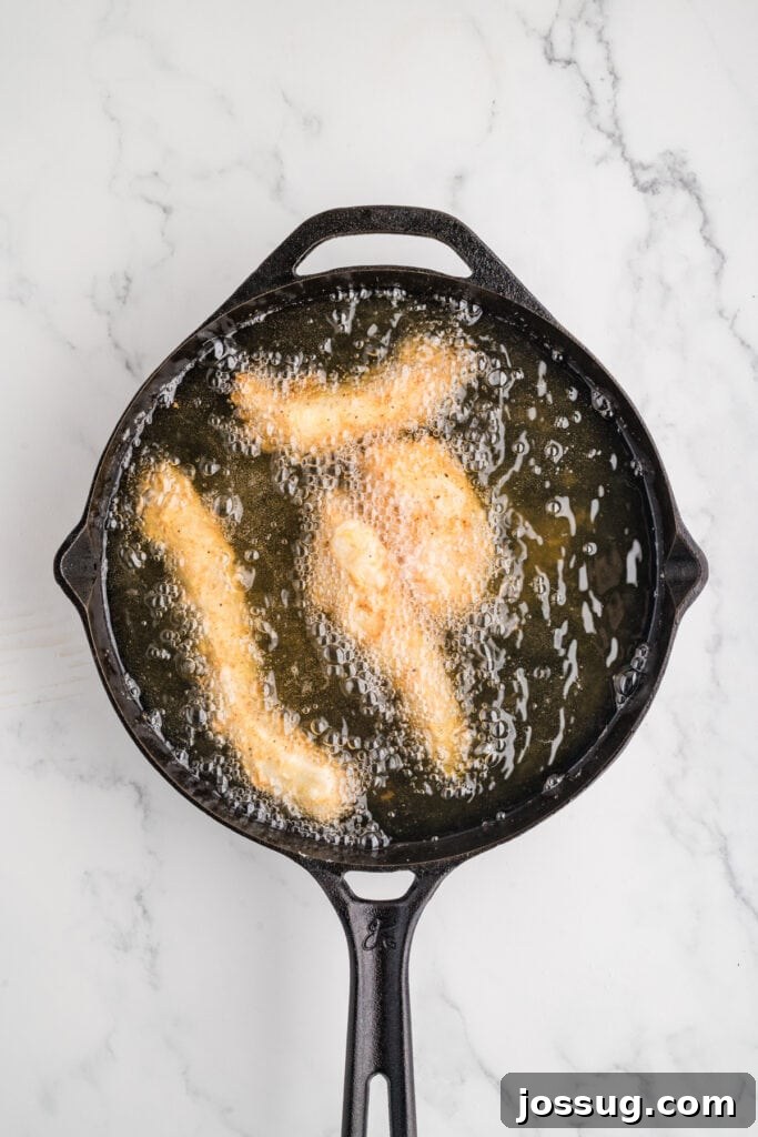 Effortless Crispy Chicken Strips for Busy Families 11 Several delectable chicken strips frying to a perfect golden brown in bubbling hot oil within a sturdy cast iron skillet, showcasing the crisping process as they cook.
