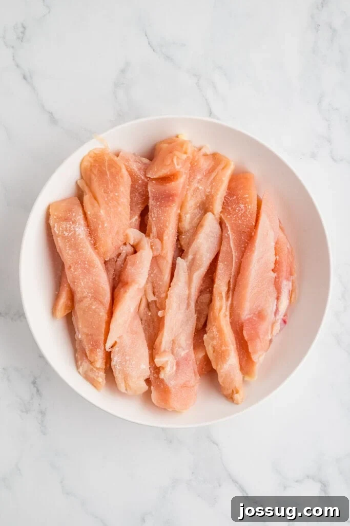 Effortless Crispy Chicken Strips for Busy Families 5 Raw chicken strips in a bowl, lightly seasoned with kosher salt, glistening and ready for the next crucial step in the preparation process.