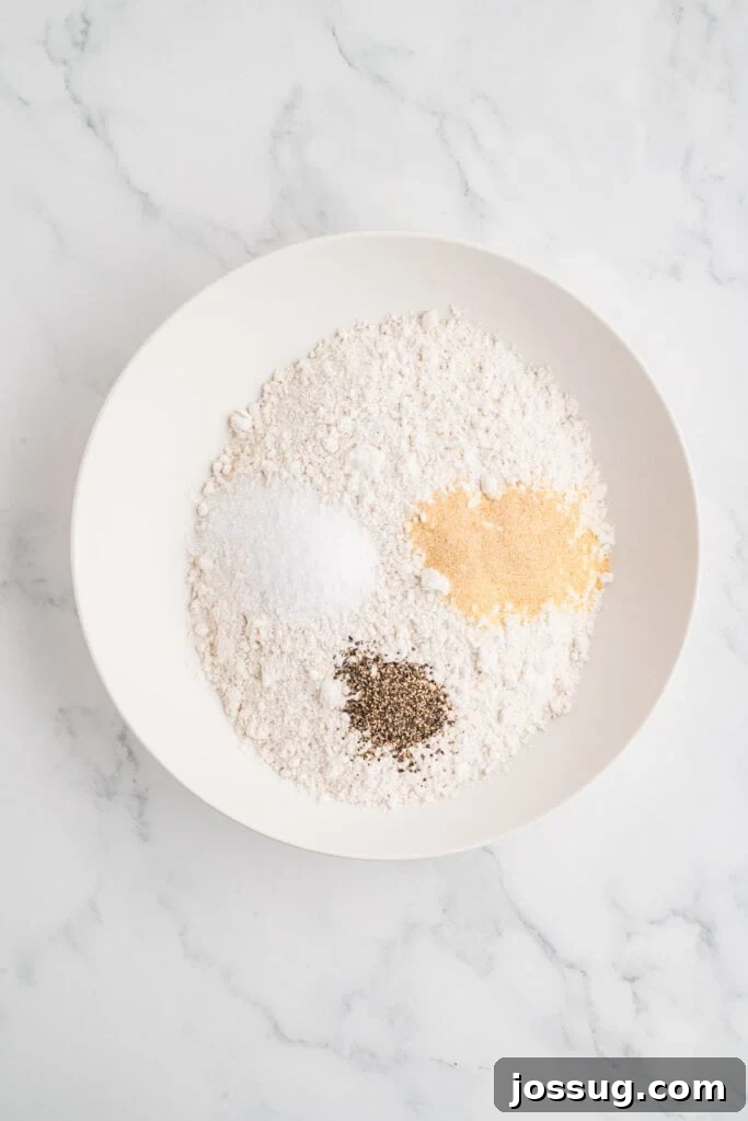 Effortless Crispy Chicken Strips for Busy Families 6 A crisp, clean image of a bowl filled with all-purpose flour, meticulously seasoned with kosher salt, coarse ground black pepper, onion powder, and garlic powder, perfectly prepared for the dry dredging step.