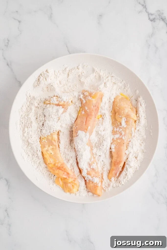 Effortless Crispy Chicken Strips for Busy Families 10 Chicken strips, now fully coated in the second layer of seasoned flour, resting in a bowl, perfectly prepared and ready for the hot oil and frying process, showcasing the thick double-dredged texture.