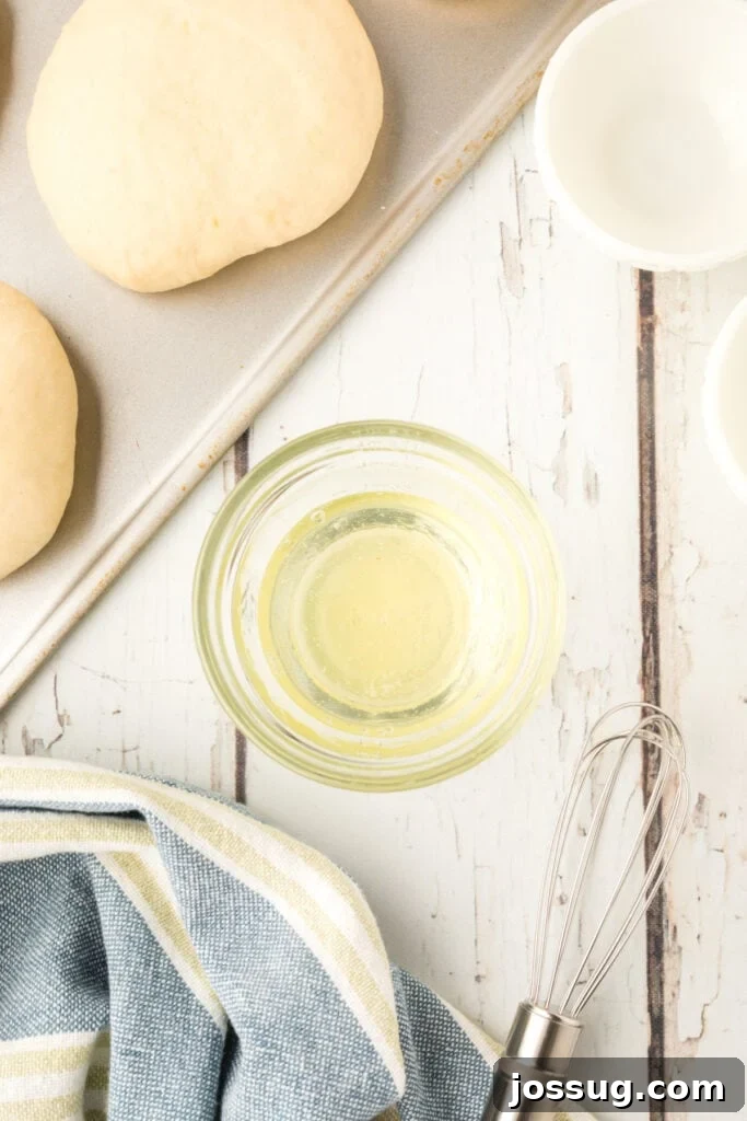 egg wash in a small bowl with a whisk next to homemade onion rolls dough on a baking sheet
