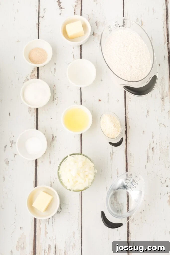 ingredients for homemade onion rolls including flour, butter, chopped onion, yeast, egg white, potato flakes, salt, sugar, and water on a white wooden surface