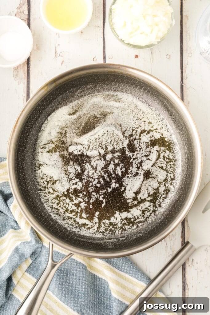 melted butter in a skillet with chopped onion and ingredients nearby on a white wooden surface