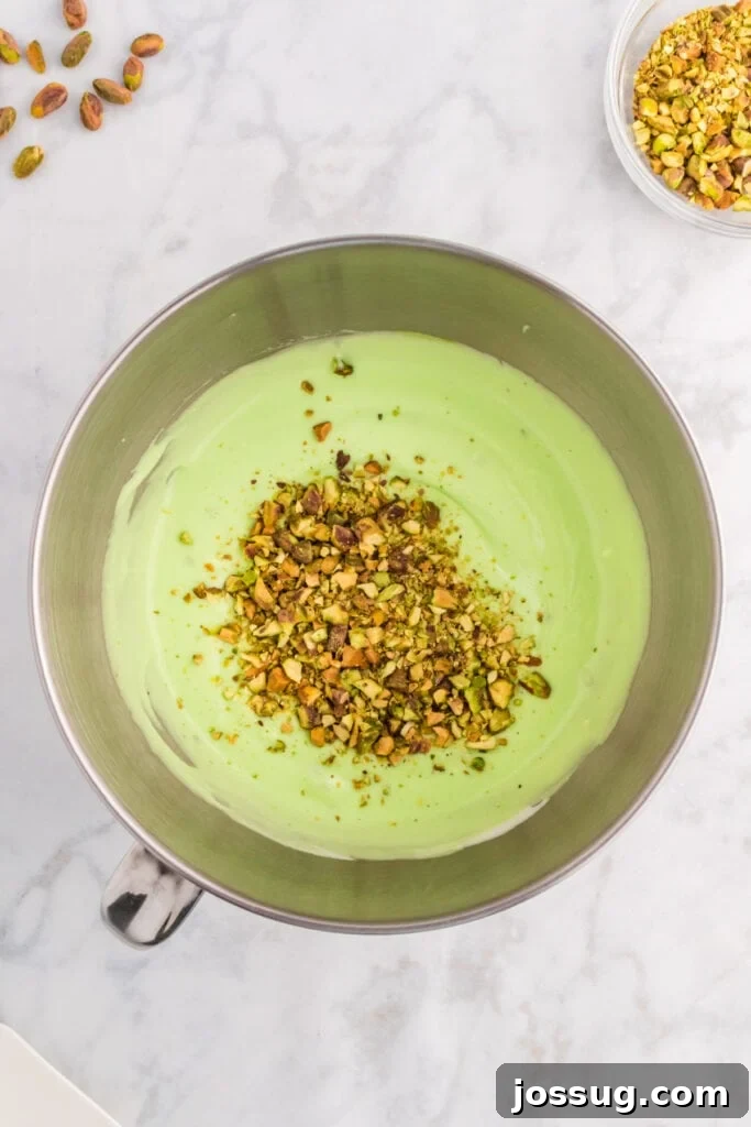 Quick No Bake Pistachio Delight 13 Finely chopped pistachios are generously stirred into the vibrant green pistachio filling mixture in a mixing bowl, adding delightful texture and intense flavor.