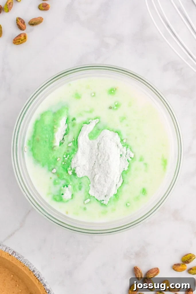 Quick No Bake Pistachio Delight 5 A bowl illustrating the initial step of combining cold milk, instant pistachio pudding mix, and a few drops of green food coloring, showing the mixture beginning to transform.