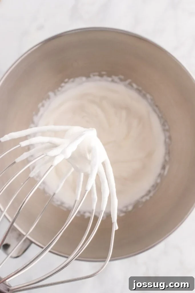 Quick No Bake Pistachio Delight 7 A whisk attachment elegantly lifting from a bowl of perfectly whipped heavy cream, showcasing the soft peaks that have formed, ready for folding.