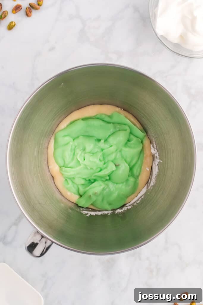 Quick No Bake Pistachio Delight 10 The vibrant pistachio pudding mixture has just been added to the creamy, beaten cream cheese mixture in a mixing bowl, preparing for the gentle folding process.