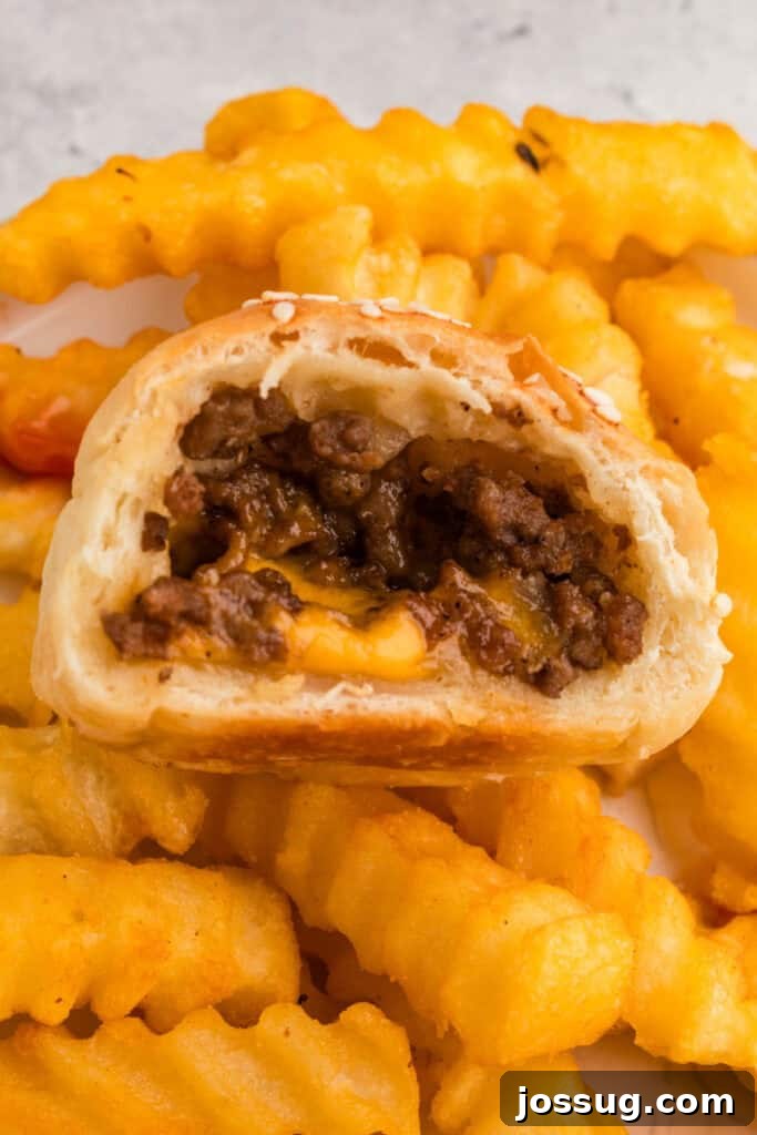 half of a burger bomb with ground beef and melted cheese served with crinkle cut fries in the background