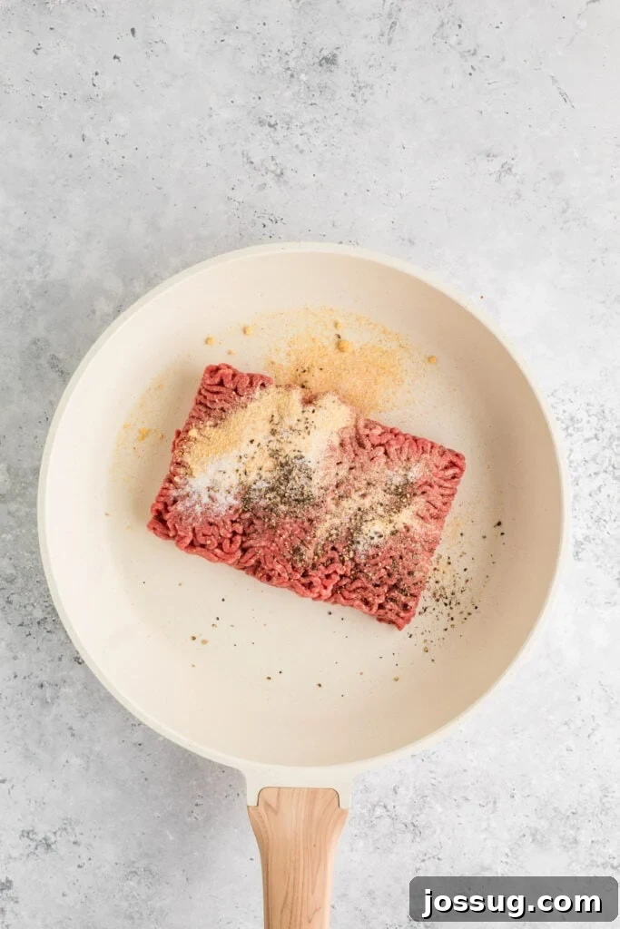 raw ground beef in a skillet with garlic powder, onion powder, salt, and pepper on top