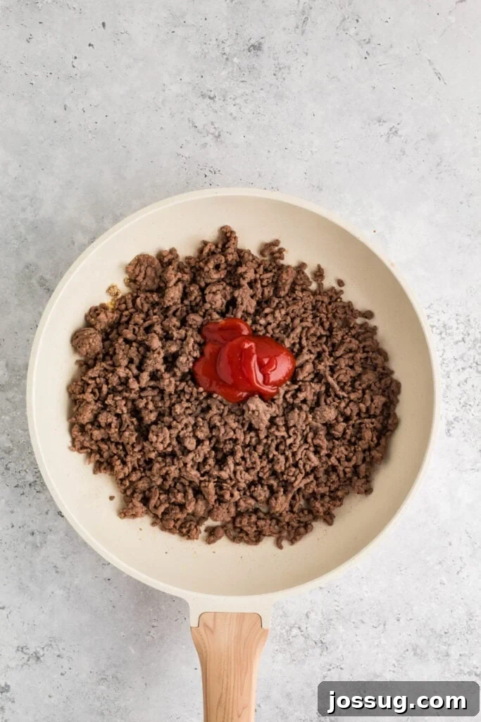 cooked ground beef in a skillet with ketchup added on top