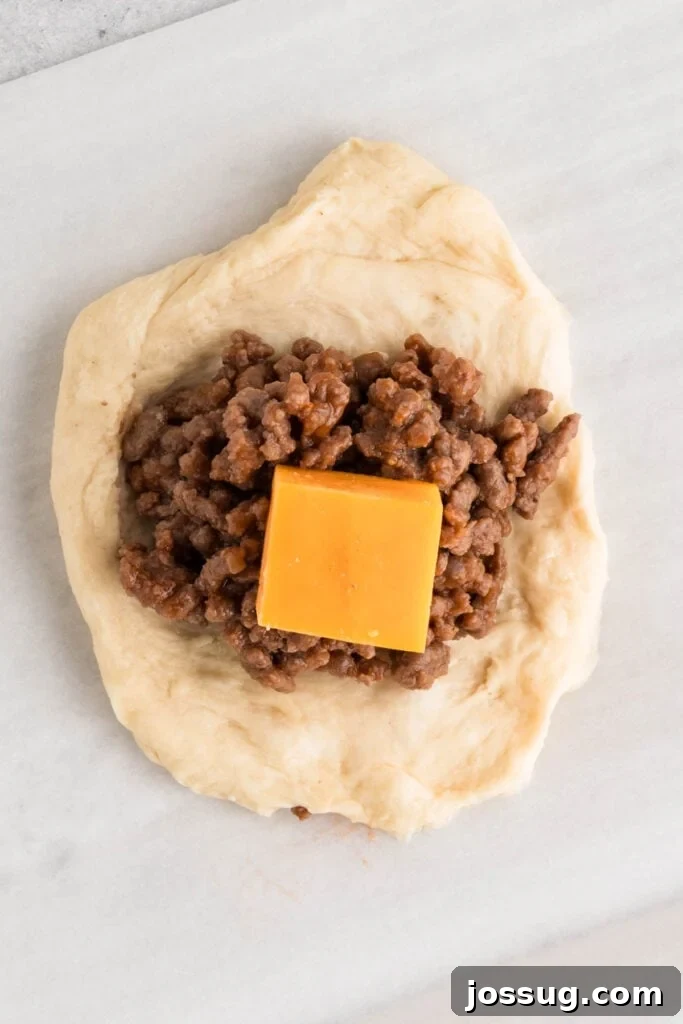 flattened dough with cooked ground beef and a cube of cheddar cheese in the center