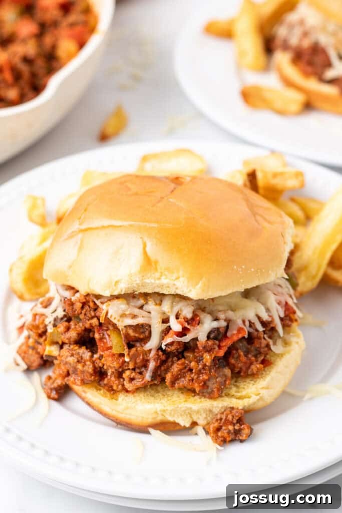 Easy Ground Beef Pizza Sloppy Joes 2 close up of Pizza Sloppy Joes sandwich with melted mozzarella on a hamburger bun served with fries on a white plate