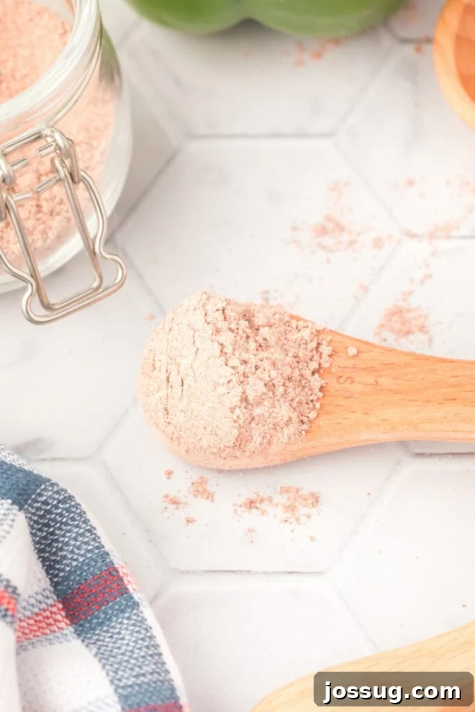 A wooden spoon filled with homemade fajita seasoning, resting beside a glass storage jar.