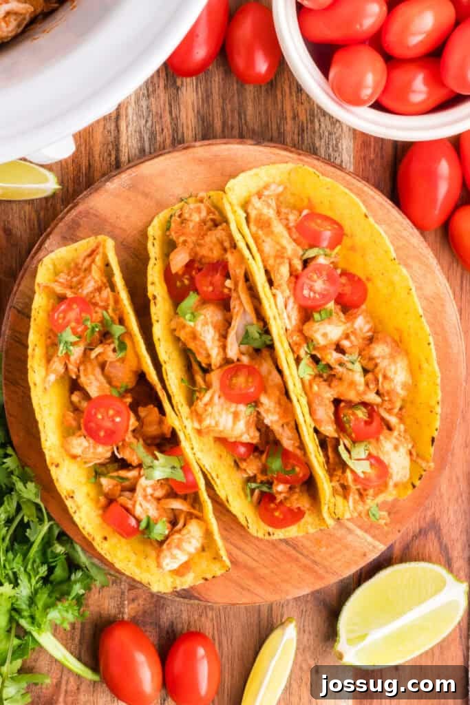 Crockpot Shredded Chicken Tacos Recipe for Busy Weeknights 11 Three Crockpot Shredded Chicken Tacos on a wooden plate with cherry tomatoes, cilantro, and lime wedges