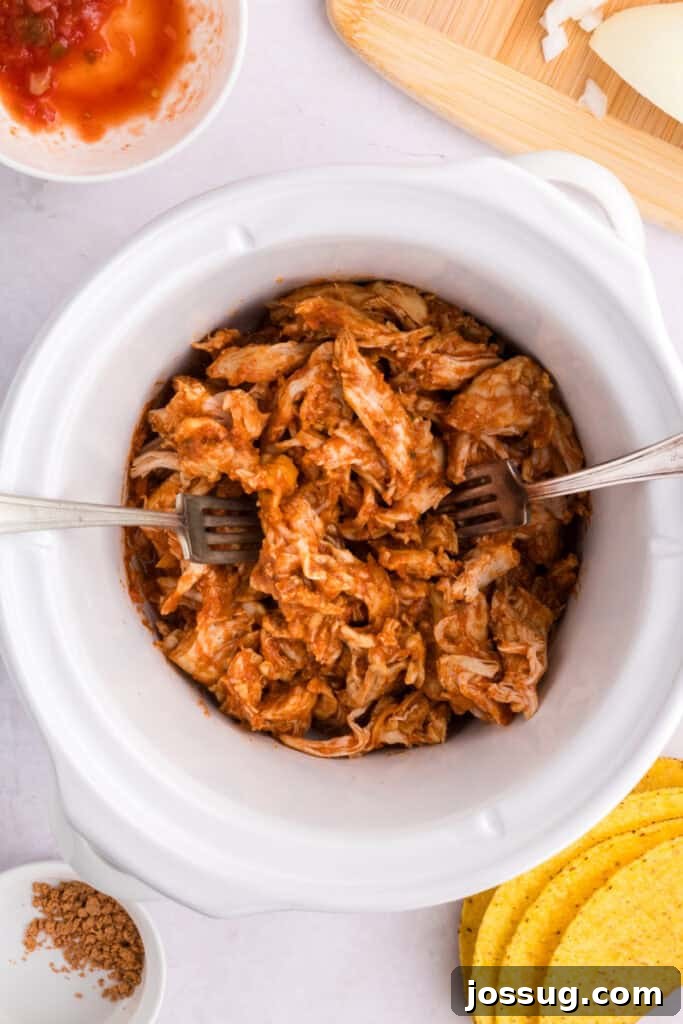 Crockpot Shredded Chicken Tacos Recipe for Busy Weeknights 10 Shredded taco chicken mixed in sauce inside a slow cooker for Crockpot Shredded Chicken Tacos