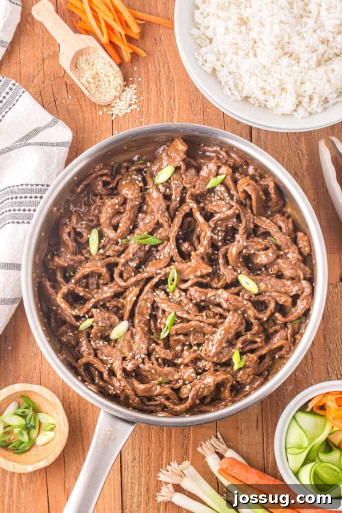 Korean Beef Bulgogi in a skillet topped with sesame seeds and green onions served with white rice and vegetables