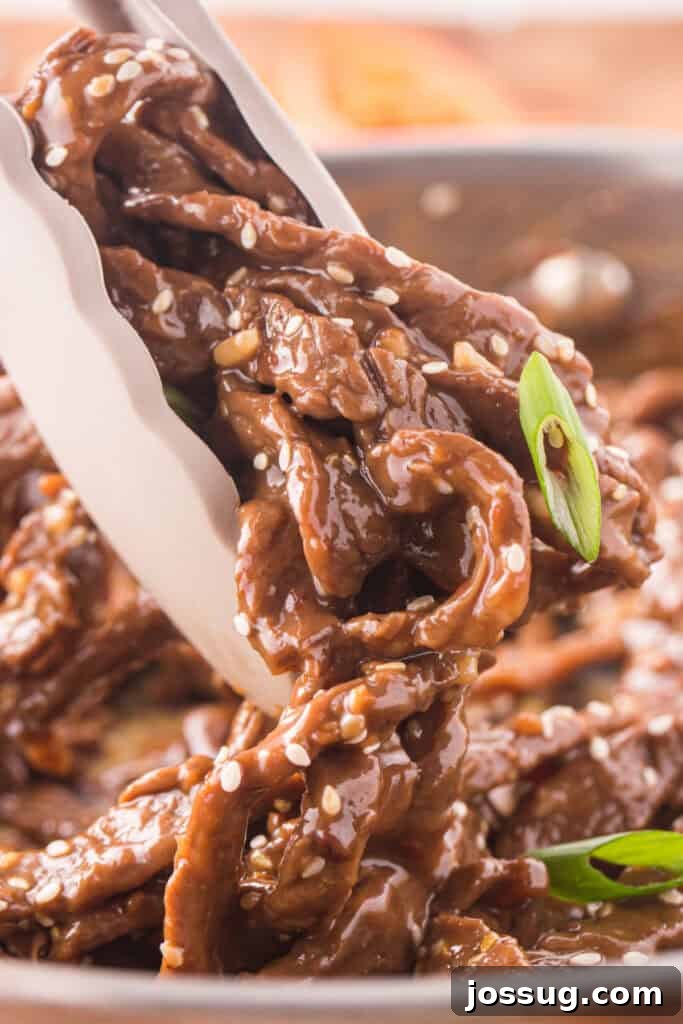 Close-up of Korean Beef Bulgogi being lifted with tongs showing thick glossy bulgogi sauce and sesame seeds