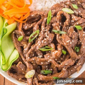 Square image of Korean Beef Bulgogi served with white rice, cucumber ribbons, carrots, sesame seeds, and green onions