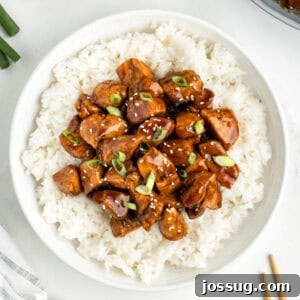 Chicken Teriyaki served over white rice with sesame seeds and sliced green onions in a white bowl