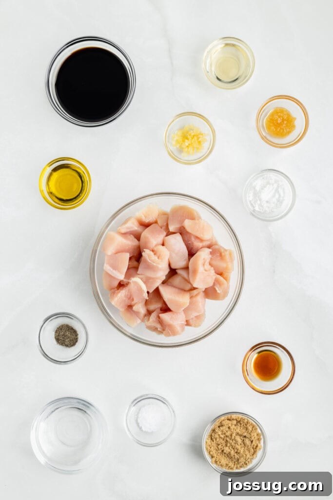 Ingredients for Chicken Teriyaki arranged on a white surface with raw chicken, soy sauce, garlic, ginger, brown sugar, and sesame oil