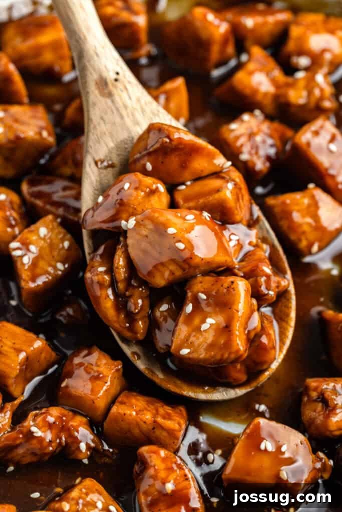 Wooden spoon holding saucy Chicken Teriyaki pieces with sesame seeds