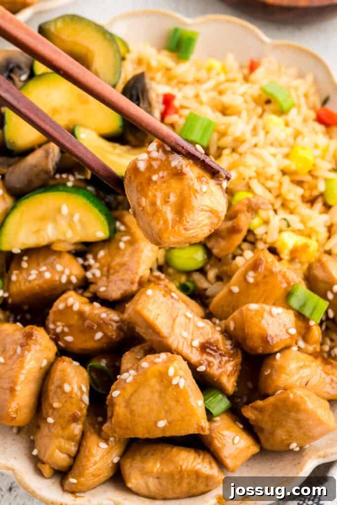 Homemade Hibachi Chicken: Restaurant-Style Recipe You’ll Love 14 Chopsticks holding a piece of Hibachi Chicken over fried rice and hibachi vegetables with sesame seeds and green onions.
