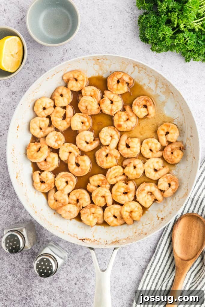 Copycat Hibachi Shrimp Recipe: Restaurant-Style at Home 13 Cooked Hibachi Shrimp coated in garlic butter sauce in a white skillet.