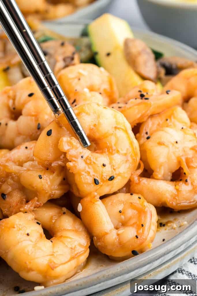 Copycat Hibachi Shrimp Recipe: Restaurant-Style at Home 14 Chopsticks holding a piece of Hibachi Shrimp above a plate of shrimp and hibachi vegetables.