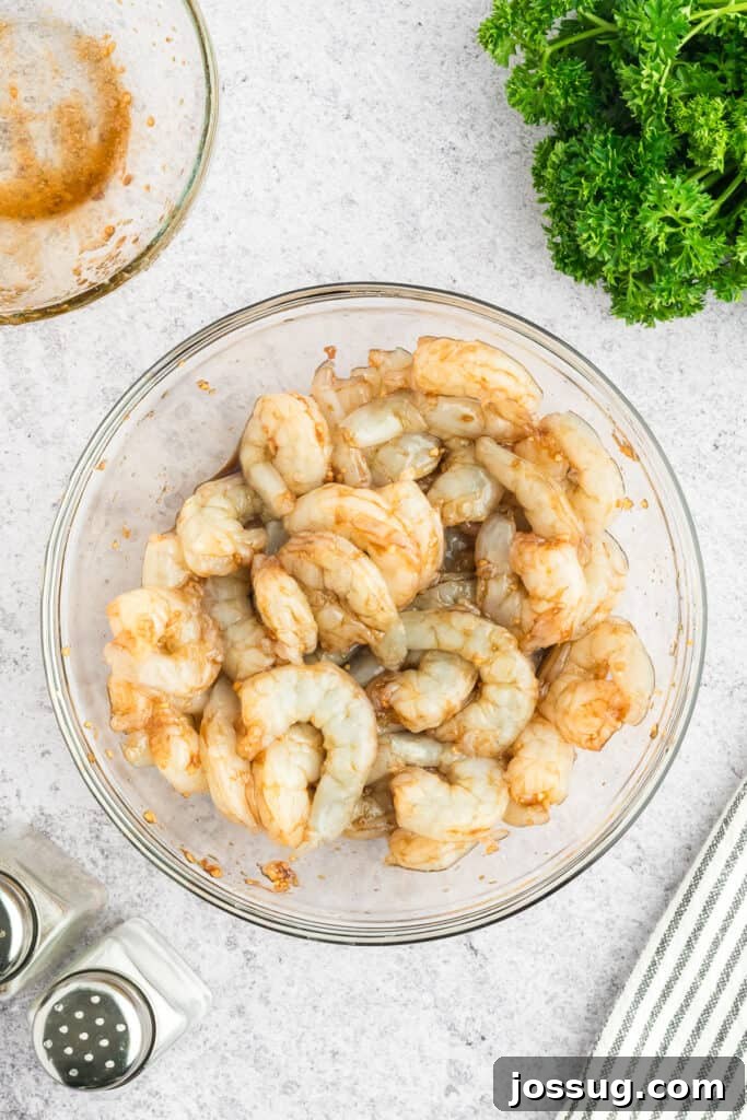 Copycat Hibachi Shrimp Recipe: Restaurant-Style at Home 8 Raw shrimp coated in Hibachi Shrimp marinade in a glass mixing bowl.