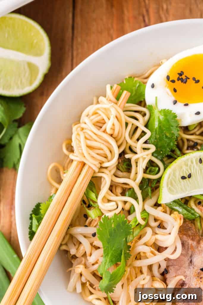 Instant Pot Pork Ramen Recipe: Homemade Broth in 30 Minutes 13 Close-up of chopsticks lifting ramen noodles from a bowl of Instant Pot Ramen topped with soft-boiled egg, bean sprouts, cilantro, green onions, lime wedge, and sliced pork
