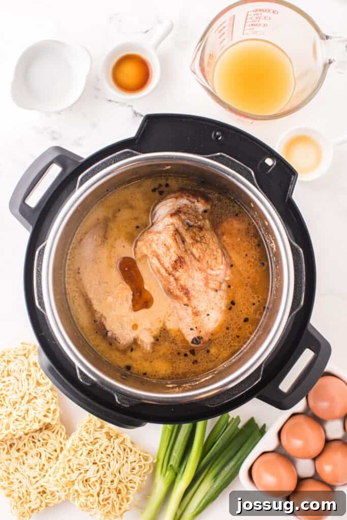 Instant Pot Pork Ramen Recipe: Homemade Broth in 30 Minutes 7 Browned pork shoulder in broth inside an Instant Pot with ramen noodles, eggs, and green onions nearby