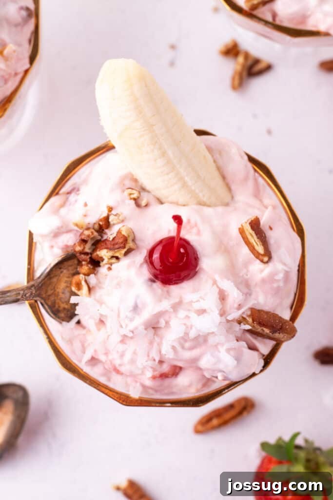 Overhead close-up of Banana Split Salad topped with coconut, pecans, a maraschino cherry, and a banana half in a dessert dish.