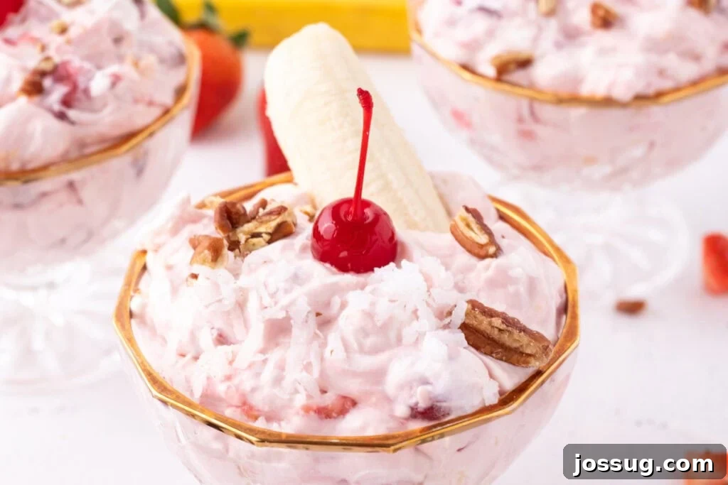 Individual serving of Banana Split Salad topped with coconut, pecans, a maraschino cherry, and a banana half in a dessert dish.