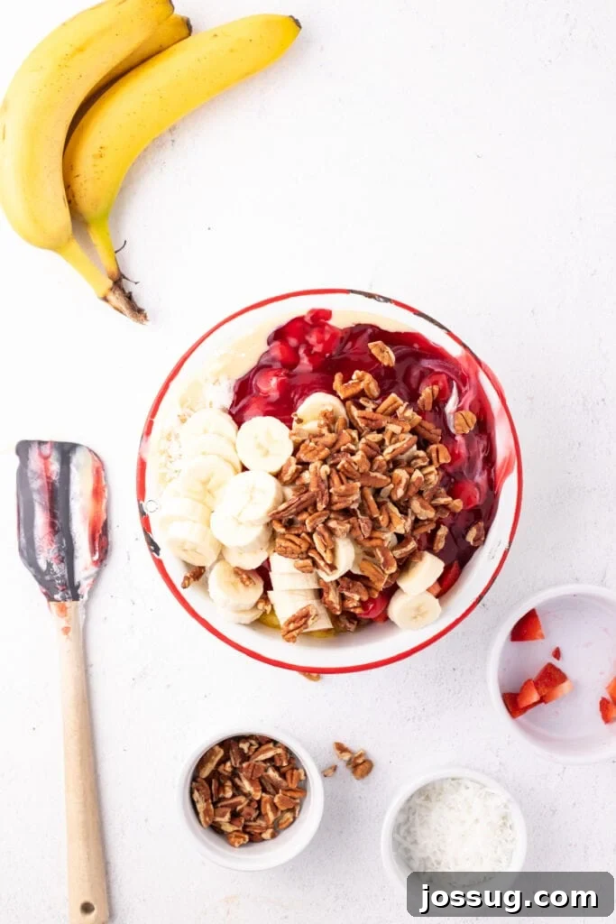 Chopped pecans added to a bowl of Banana Split Salad ingredients before stirring together.