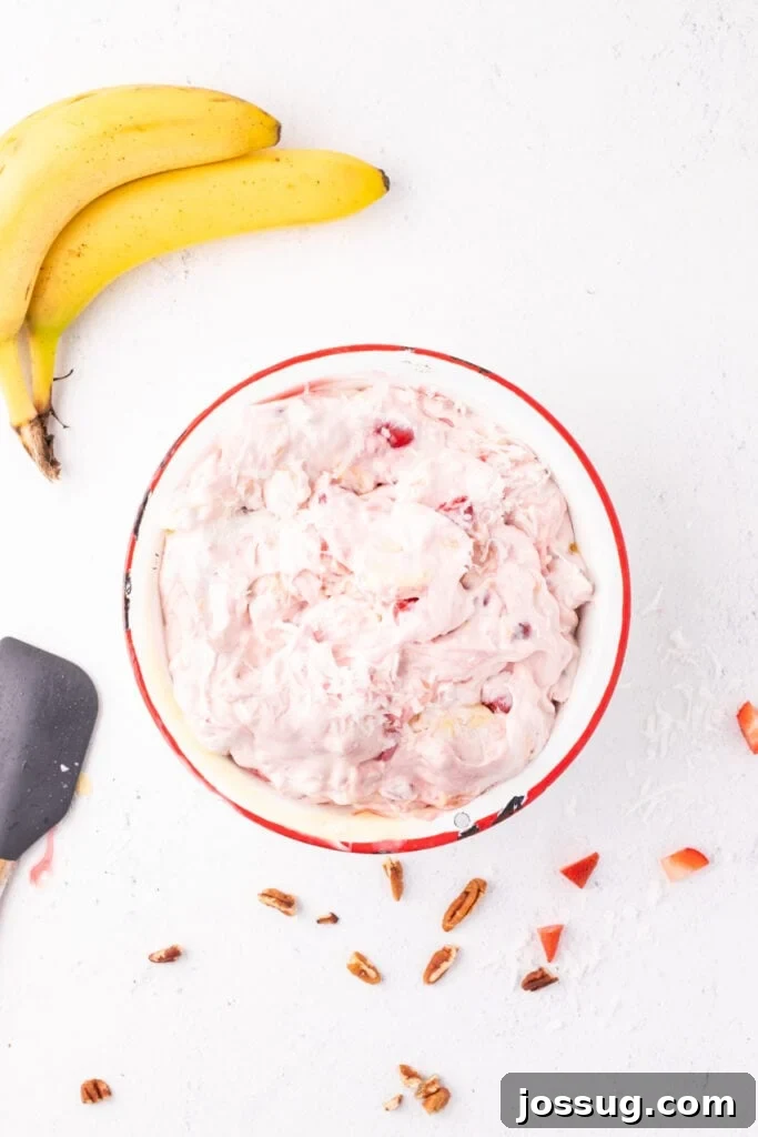Mixed Banana Split Salad in a bowl with visible strawberries, bananas, coconut, and cherries in a creamy pink filling.
