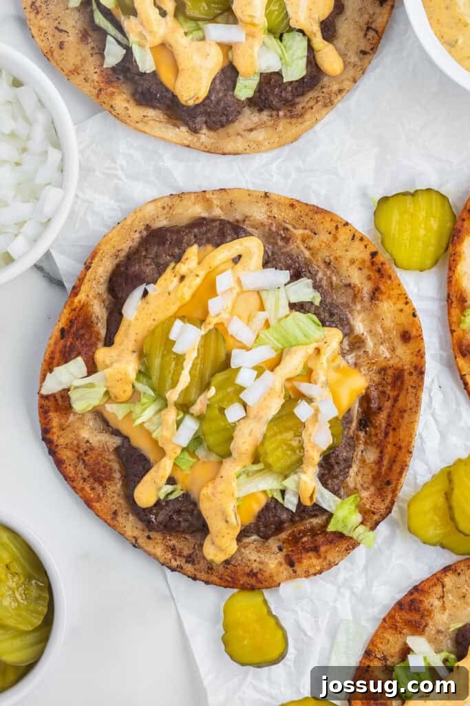 Smash Burger Tacos: Viral Cheeseburger-Style Taco Recipe 2 Overhead view of a Smash Burger Taco topped with melted cheese, burger sauce, lettuce, onions, and pickle slices.