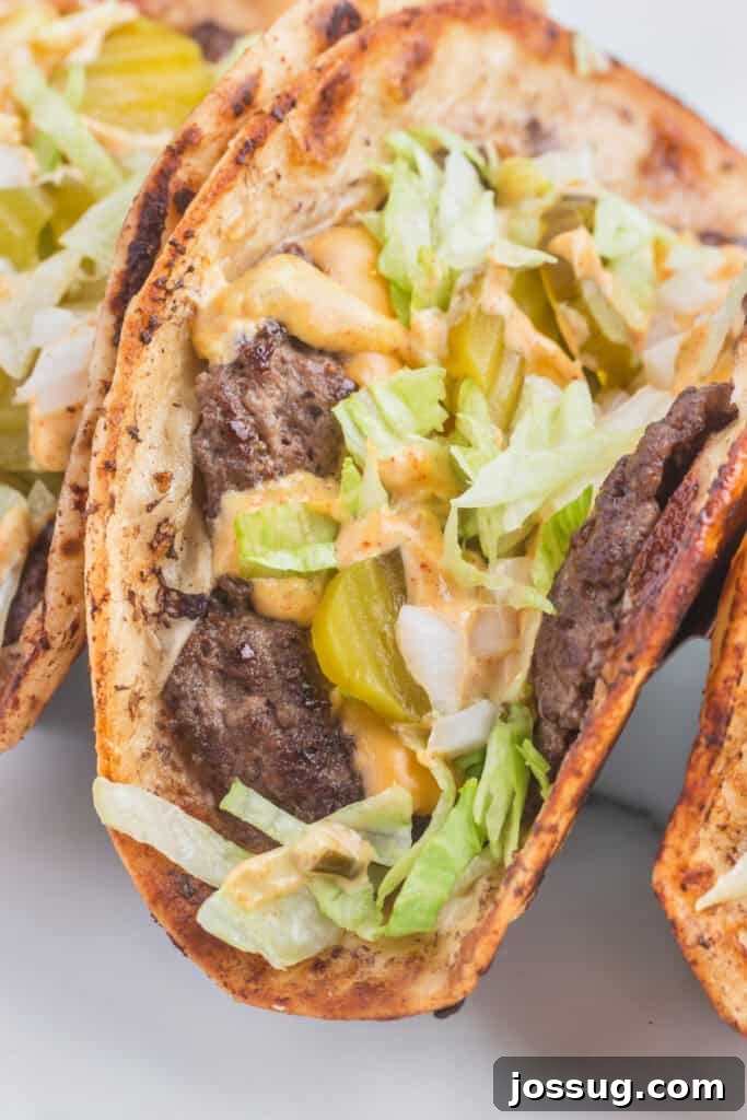 Smash Burger Tacos: Viral Cheeseburger-Style Taco Recipe 9 Close-up of a folded Smash Burger Taco filled with seasoned beef, melted cheese, burger sauce, shredded lettuce, diced onion, and pickles.