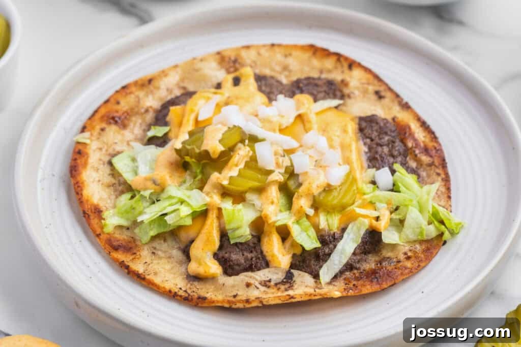 Smash Burger Tacos: Viral Cheeseburger-Style Taco Recipe 4 Smash Burger Taco on a plate topped with melted American cheese, burger sauce, shredded lettuce, diced onion, and pickle slices.