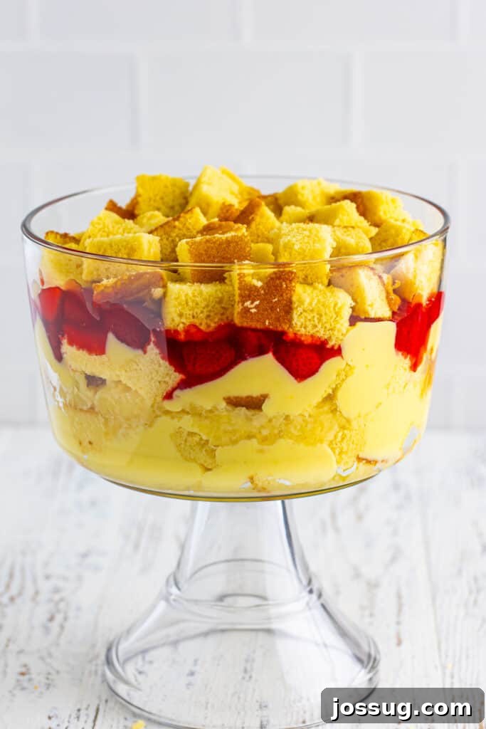 Decadent Banana Split Trifle Recipe with Layers of Cream and Fruit 13 Additional layer of cubed yellow cake added on top of strawberry pie filling in a clear trifle bowl for Banana Split Trifle.