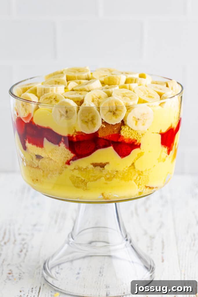 Decadent Banana Split Trifle Recipe with Layers of Cream and Fruit 15 Sliced bananas arranged over the pudding layer in a clear trifle bowl for Banana Split Trifle.